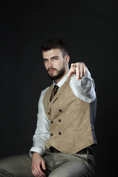 closeup portrait of the beautiful charismatic young man with a beard wearing pants, shirt, vest and tie on a dark background studio  - Foto, Imagem