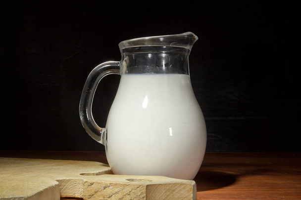 Glass jug with fresh milk on a wooden table - Fotoğraf, Görsel