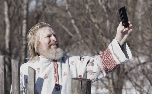 Slavic man in a beautiful national painted shirt on a spring day on the earth makes selfy - Foto, Imagem