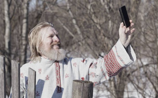 Slavic man in a beautiful national painted shirt on a spring day on the earth makes selfy - Valokuva, kuva