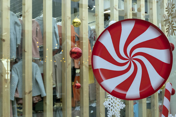 Un grand cercle avec un motif en spirale rouge et blanche, des boules de Noël et un flocon de neige pendent sur le fond d'une vitrine avec des vêtements. Résumé Décor du Nouvel An dans le magasin. Le concept de thème des achats de vacances
. - Photo, image