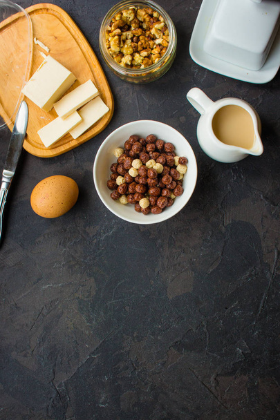 Cornflakes, Kaffee, Quark, Brot, Butter, Eier, Marmelade und andere Zutaten zum Frühstück auf dunklem Hintergrund. Ansicht von oben mit Kopierraum - Foto, Bild