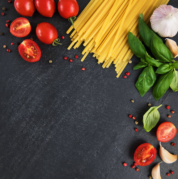 Italian food ingredients. Pasta, tomatoes, basil and spices on a black background - Photo, Image