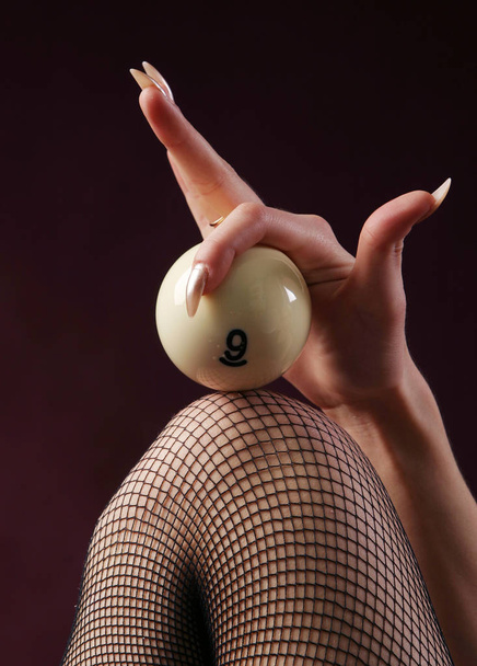 close-up on a woman's knee in a stocking clad ivory billiard ball on a burgundy background studio - Fotoğraf, Görsel