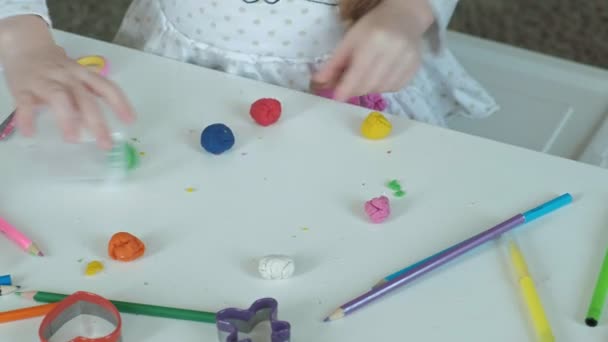 Gelukkig klein meisje zet veelkleurige plasticine in een container, op het bureaublad zijn cijfers en kleurpotloden, de ontwikkeling van de fijne motoriek van handen - Video