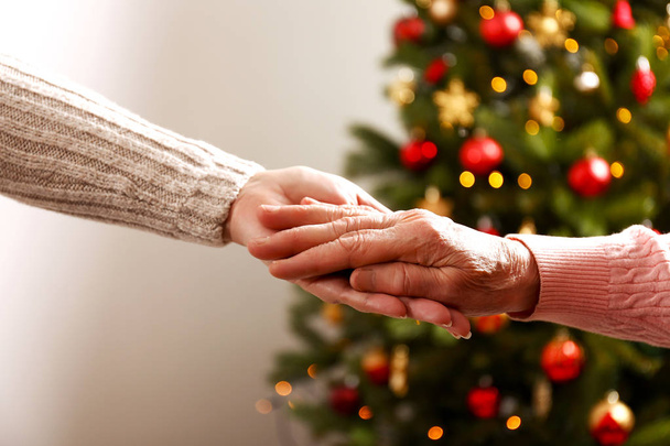 Elderly woman celebrating Christmas at home, with decorated holiday pine tree on background. Old lady at nursing home. Close up, copy space, cropped shot. - 写真・画像