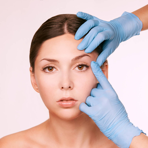 Beautiful white girl. Medical gloves near face. Cosmetology procedure. - Photo, Image