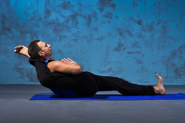 Young man practicing yoga in a posture lying leg behind his head - Fotó, kép