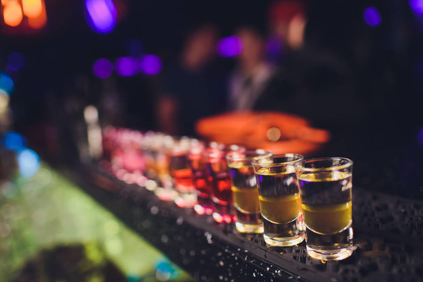 Variation of hard alcoholic shots served on bar counter. Blur bottles on background. - Photo, Image