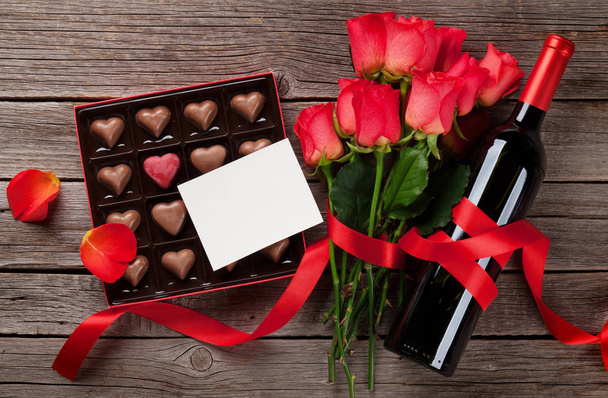 День Святого Валентина с красными розами, бутылкой вина и шоколадом на деревянном столе. Вид сверху с пространством для вашего текста
 - Фото, изображение