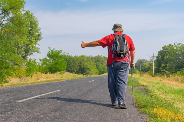 Senior autoestopista caminando en una carretera en el área rural ucraniana en la hora de verano
 - Foto, Imagen