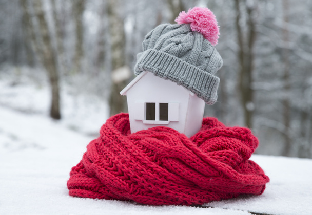 Haus im Winter - Heizungskonzept und kaltes, schneereiches Wetter mit Modell eines Hauses mit Strickmütze - Foto, Bild