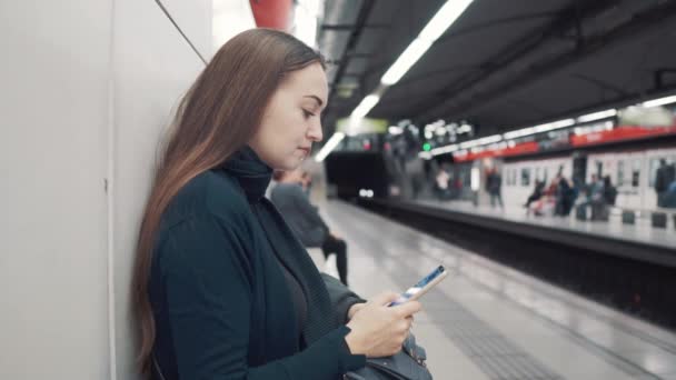 Vrouw typen op smartphone bij metrostation. Wachten op trein - Video
