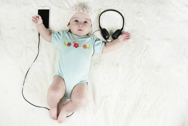 Bright little beautiful newborn baby lying on the bed listening to music and next to the headset with the phone close-up - Foto, imagen