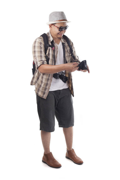 Traveling people concept. Portrait of Asian male backpacker tourist wearing hat, black sunglasses, camera and backpack isolated on white. Full body portrait. Broke empty wallet - Fotó, kép