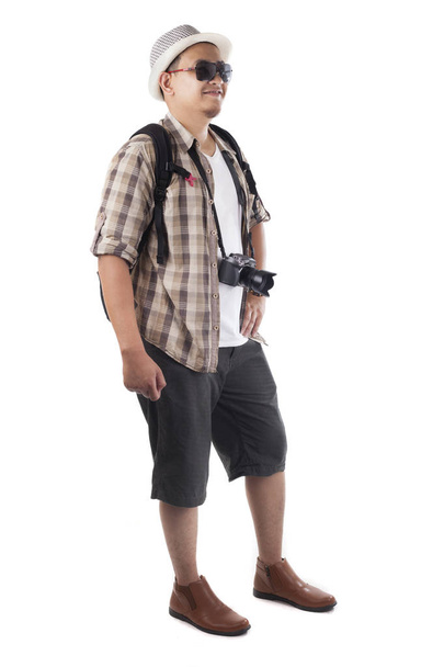 Traveling people concept. Portrait of Asian male backpacker tourist wearing hat, black sunglasses, camera and backpack isolated on white. Full body portrait. Smiling happy gesture - Photo, image