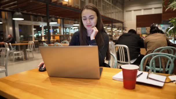 Menina jovem e bonita trabalhando com laptop e beber café em uma mesa de madeira
 - Filmagem, Vídeo