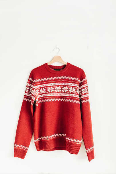 Теплый красный свитер на вешалке на белом фоне. Концепция моды на Рождество, Новый год, зиму
. - Фото, изображение