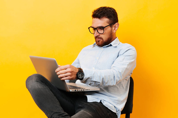 Чоловік сидить на стільці і дивиться на ноутбук на жовтому тлі
 - Фото, зображення