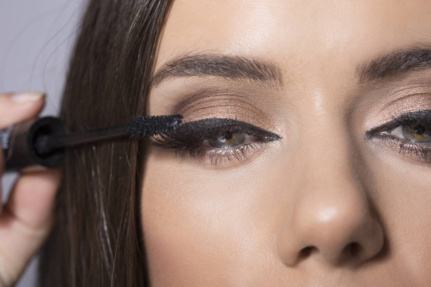 Young brunette woman putting mascara on eyelashes - Valokuva, kuva