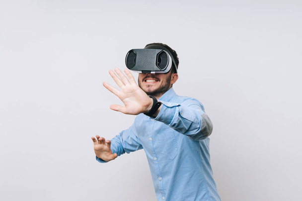Χαρούμενος νεαρός άνδρας στο casual έχοντας εικονική εμπειρία πάνω από το λευκό φόντο. VR γυαλιά - Φωτογραφία, εικόνα