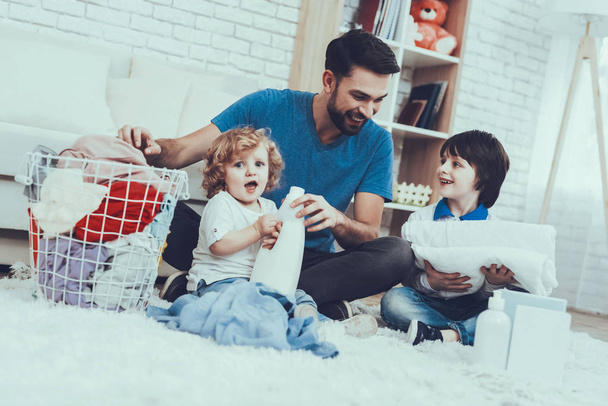 Man Spends Time with His Sons. Father is Engaged in Raising Children. Father is Teaching a Sons a Cleaning. People Want to Wash a Dirty Clothes. People is Located in Bedroom on Carpet. - Foto, Bild
