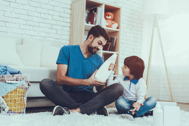 Man Spends Time with His Son. Father of Boy is Engaged in Raising Child. Father is Teaching a Son a Cleaning. Man is Holding a Cleanser. Persons is Sitting on Carpet. People is Located in Bedroom. - Foto, Imagen
