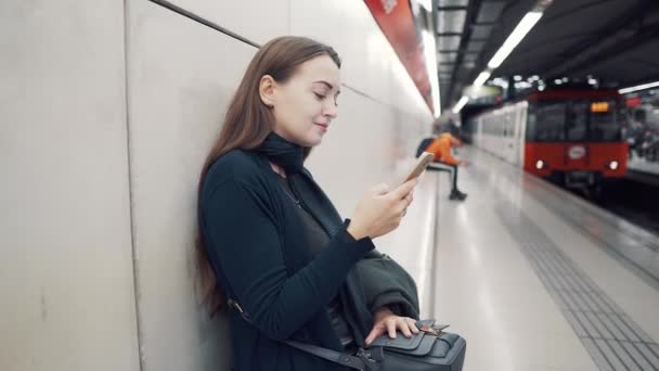 Mujer escribiendo en el teléfono inteligente en la estación de metro. Esperando el tren
 - Imágenes, Vídeo