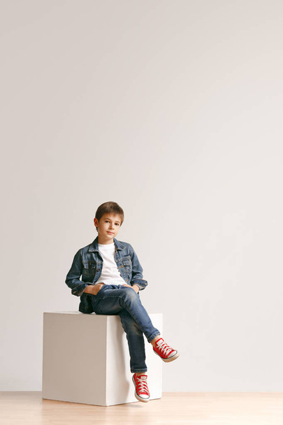 The portrait of cute little boy in stylish jeans clothes looking at camera at studio - Фото, изображение