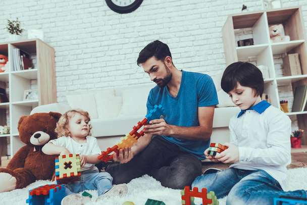 Man Spends Time with His Sons. Father is Engaged in Raising Children. Father and Sons is Playing with Toys. Eldest Son is Holding a Rubik's Cube. Persons is Sitting on Carpet in Bedroom. - Φωτογραφία, εικόνα