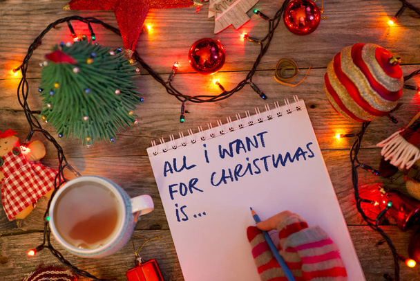All I want for karácsony a szöveget írta fiatal nő az ünnepi dekoráció színes kesztyűben notebook  - Fotó, kép