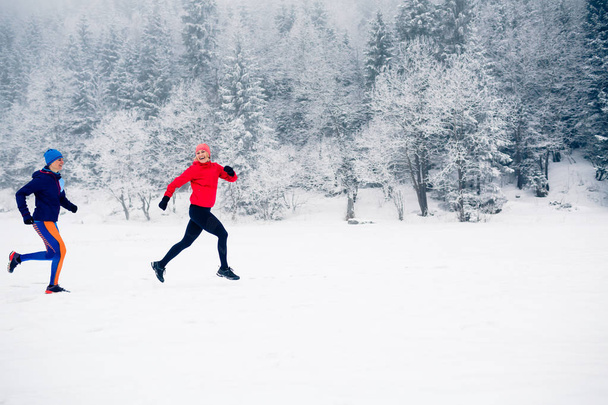 Tytöt juoksevat yhdessä lumella talvivuorilla. Urheilu, kunto inspiraatiota ja motivaatiota. Kaksi naiskumppania juoksee vuorilla talvipäivänä. Nainen trail juoksija lenkkeily ulkona
. - Valokuva, kuva
