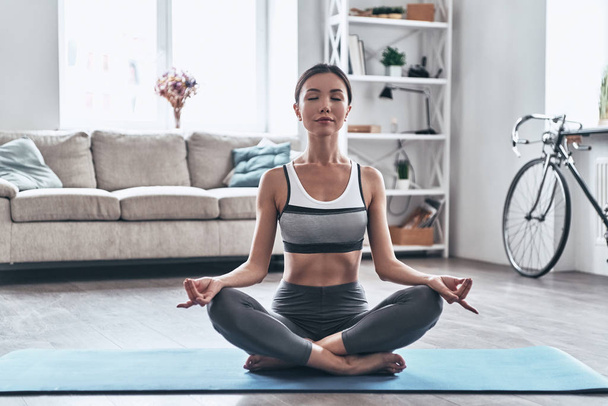 Beautiful young Asian woman in sports clothing doing yoga while relaxing at home         - Φωτογραφία, εικόνα