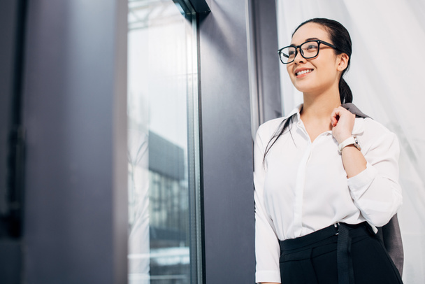 pretty businesswoman looking at window and smiling in office - Foto, Imagen