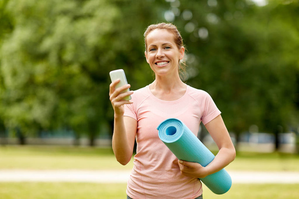 woman with exercise mat and smartphone at park - Valokuva, kuva