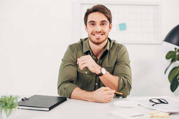 Молодий бізнесмен тримає олівець і посміхається в сучасному офісі
  - Фото, зображення