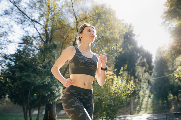 Portrait of attractive brunette female runner running in city park airpods bluetooth headphones earphones. Healthy fitness athletic woman jogging outdoors - Foto, afbeelding