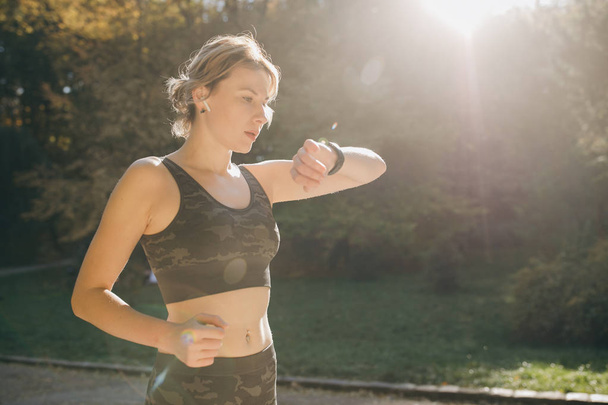Fitness Woman In Wireless Earphones Using Smartwatch and runs in morning light - Photo, image