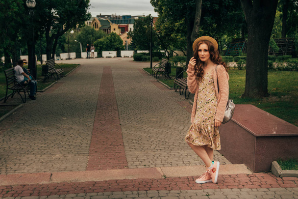 A romantic girl in the city wearing a dress and a sweater of warm colors, her hair develops in the wind. smiling and dizzy. keeps his hat on - Photo, Image