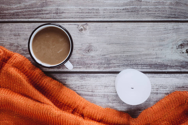 Winter cozy concept. Flat lay of orange knitted sweater, candle and coffee with milk  on wooden table - Foto, Imagem
