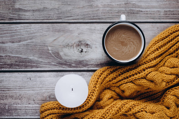 Winter cozy concept. Flat lay of orange scarf, candle and coffee with milk drink on wooden table - Φωτογραφία, εικόνα