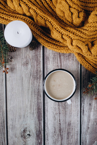 Cup of coffee  with milk, candle, bumps, spruce branches and warm orange scarf on wooden table.Winter concept. Flat lay, top view.  - Fotoğraf, Görsel