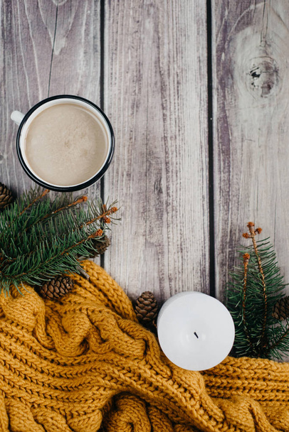 Cup of coffee  with milk, candle, bumps, spruce branches and warm orange scarf on wooden table.Winter concept. Flat lay, top view.  - Fotografie, Obrázek