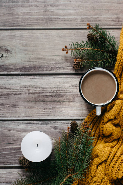 Cup of coffee  with milk, candle, bumps, spruce branches and warm orange scarf on wooden table.Winter concept. Flat lay, top view.  - Foto, Imagen