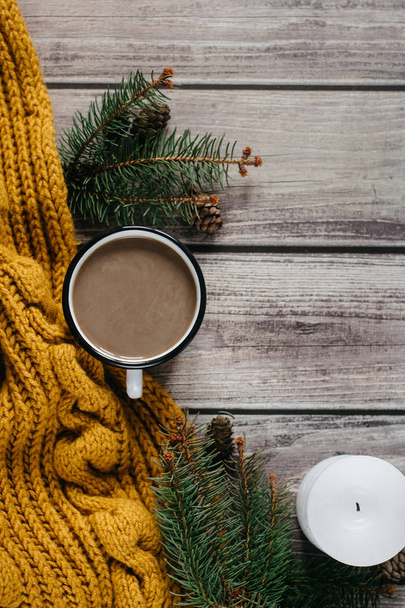 Cup of coffee  with milk, candle, bumps, spruce branches and warm orange scarf on wooden table.Winter concept. Flat lay, top view.  - Fotografie, Obrázek