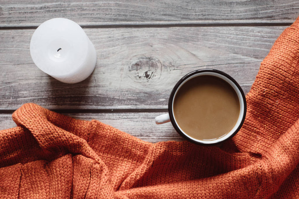 Winter cozy concept. Flat lay of orange knitted sweater, candle and coffee with milk  on wooden table - Photo, Image