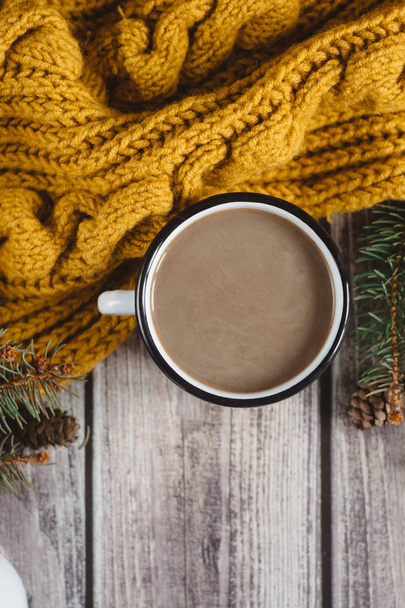 Cup of coffee  with milk, candle, bumps, spruce branches and warm orange scarf on wooden table.Winter concept. Flat lay, top view.  - Valokuva, kuva