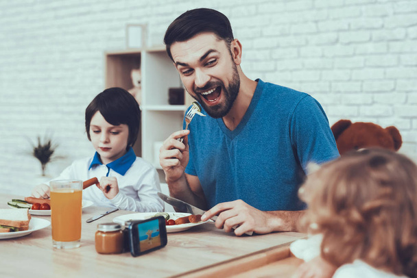 Man Spends Time with His Sons. Father of Boys is Engaged in Raising Children. Eldest Son and Father is Eating a Breakfast. Father is Smiling. People is Sitting at Table. People Located on Kitchen. - Photo, Image