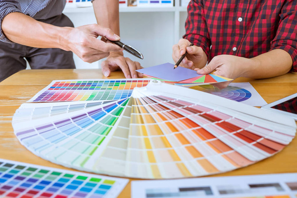 Ομαδική εργασία των νέων δημιουργικών σχεδιαστών εργάζονται σε μαζί του έργου και να επιλέξετε χρώμα swatch δειγμάτων για επιλογή χρωματισμού σε ψηφιακά γραφικά δισκίο στο χώρο εργασίας. - Φωτογραφία, εικόνα
