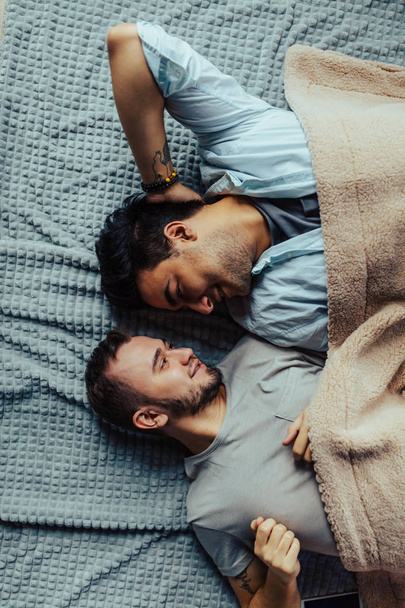 Handsome sleepy man with bristle kissing good night male partner lying in bed - Zdjęcie, obraz